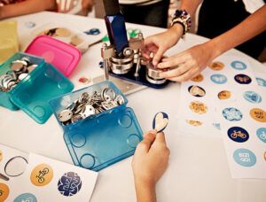 Atelier DIY avec machine badges personnalisés – enfants créant des badges avec des visuels colorés sur une table d’atelier